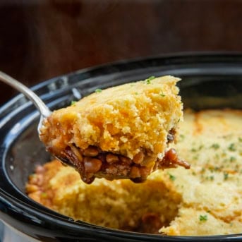 Scoop of Slow Cooker Cornbread Cowboy Casserole being held above the slow cooker.