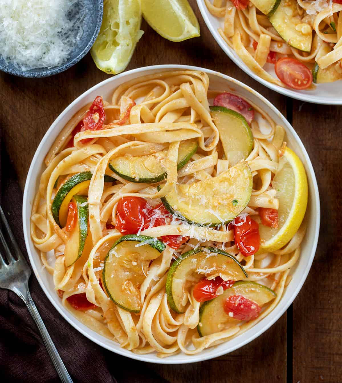 Plates of Zucchini & Blistered Tomato Fettuccine on a wooden table from overhead Plates of Zucchini & Blistered Tomato Fettuccine on a wooden table from overhead.