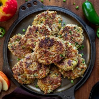 Skillet with Apple Jalapeño Breakfast Sausage Patties on it on a wooden table with apples and jalapenos.