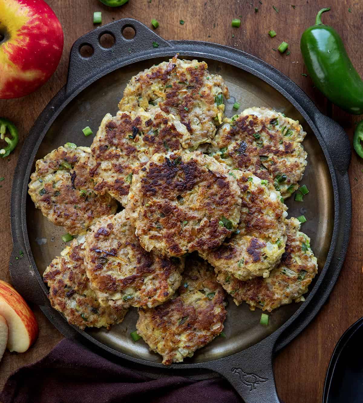 Skillet with Apple Jalapeño Breakfast Sausage Patties on it on a wooden table with apples and jalapenos Skillet with Apple Jalapeño Breakfast Sausage Patties on it on a wooden table with apples and jalapenos.