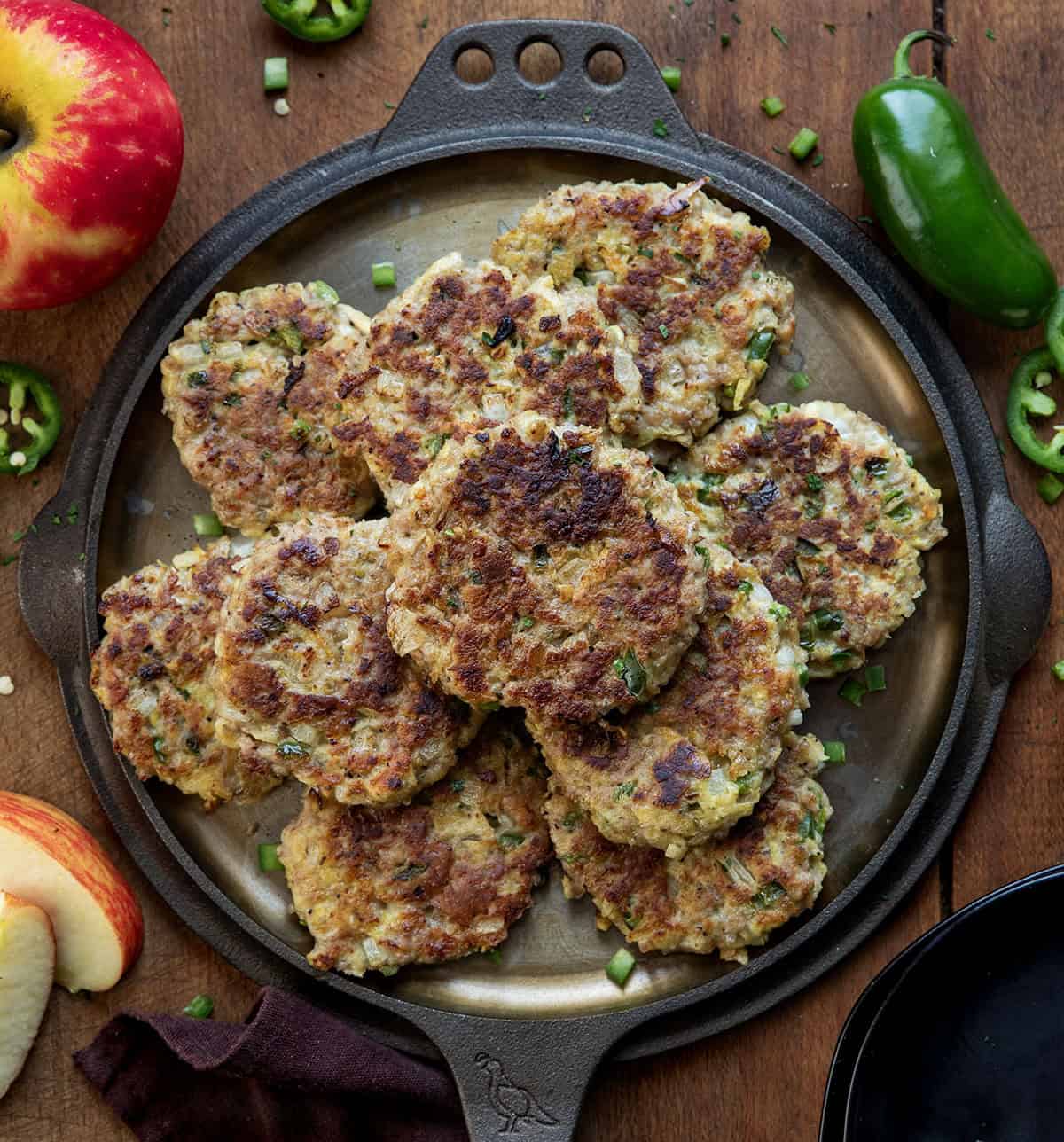 Skillet with Apple Jalapeño Breakfast Sausage Patties on it on a wooden table with apples and jalapenos Skillet with Apple Jalapeño Breakfast Sausage Patties on it on a wooden table with apples and jalapenos.