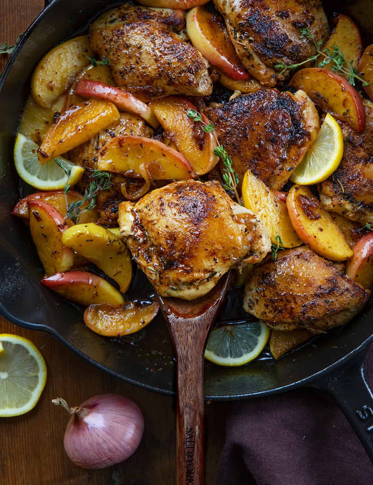 Skillet of Apple Shallot Chicken on a wooden table with a wooden spoon in the skillet Skillet of Apple Shallot Chicken on a wooden table with a wooden spoon in the skillet.