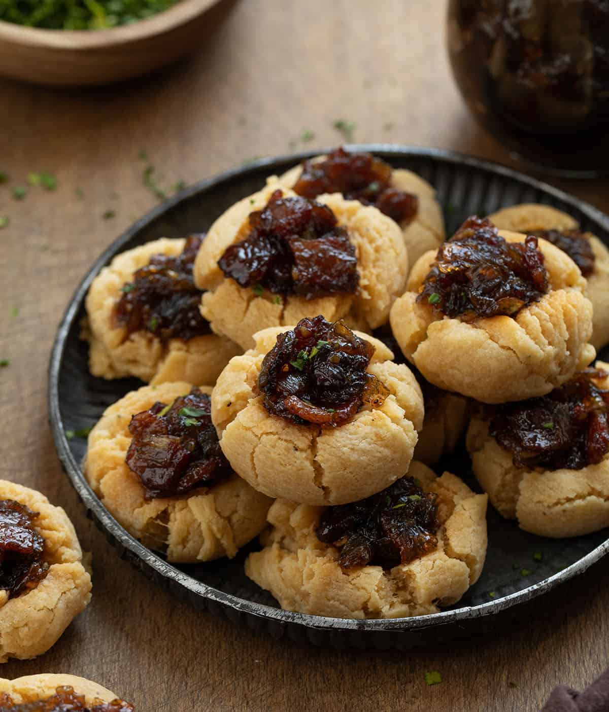 Tray of Bacon Jam Cheddar Thumbprint Cookies on a wooden table surrounded by bacon jam and more cookies Tray of Bacon Jam Cheddar Thumbprint Cookies on a wooden table surrounded by bacon jam and more cookies.