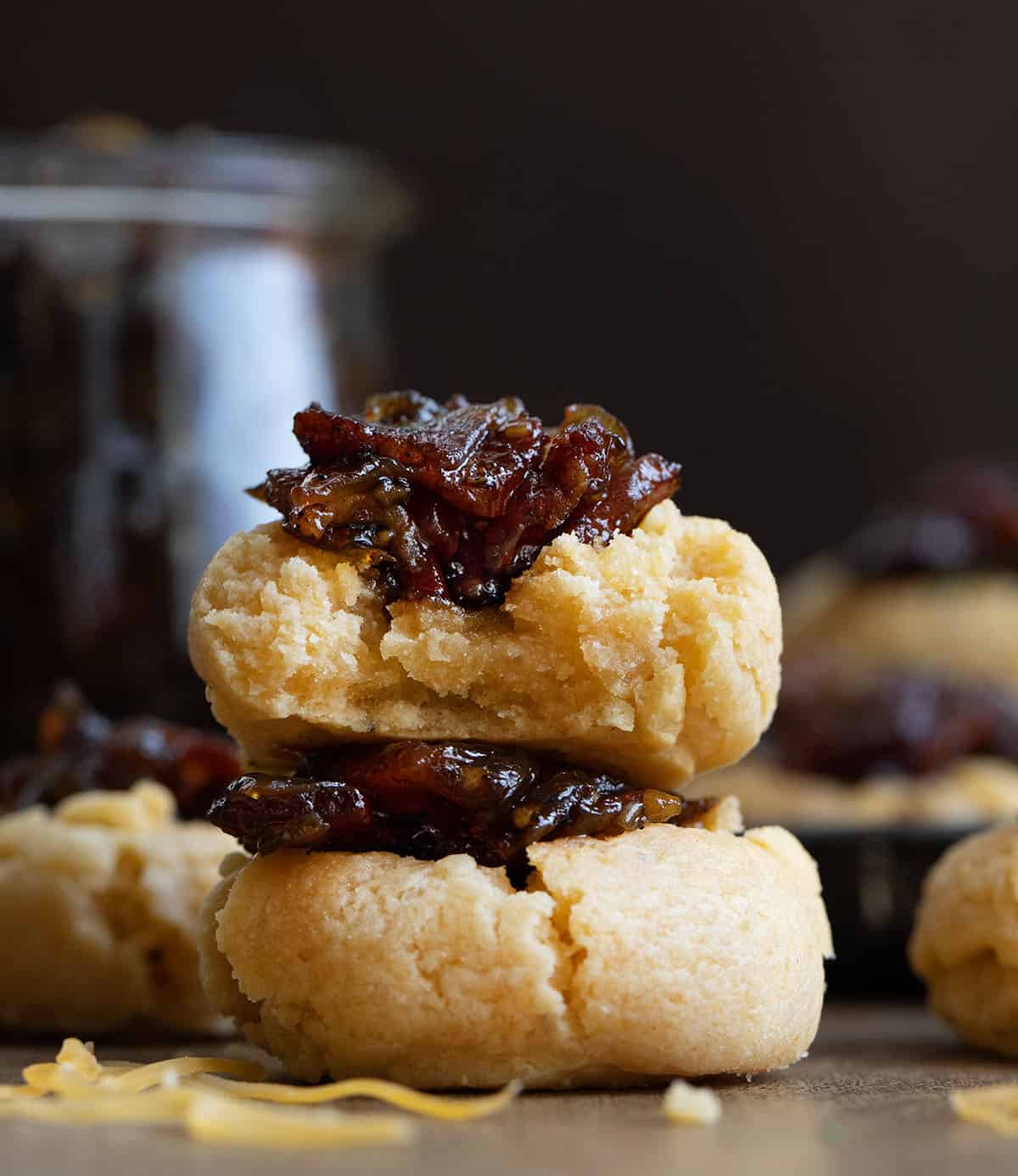 Straight on view of a stack of Bacon Jam Cheddar Thumbprint Cookies with the top cookie bit into showing the inside texture Straight on view of a stack of Bacon Jam Cheddar Thumbprint Cookies with the top cookie bit into showing the inside texture.
