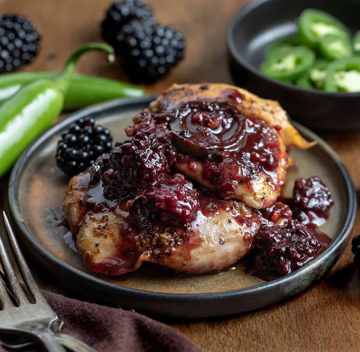Plate with Blackberry Fire Chicken on it with peppers and blackberries around it Plate with Blackberry Fire Chicken on it with peppers and blackberries around it.