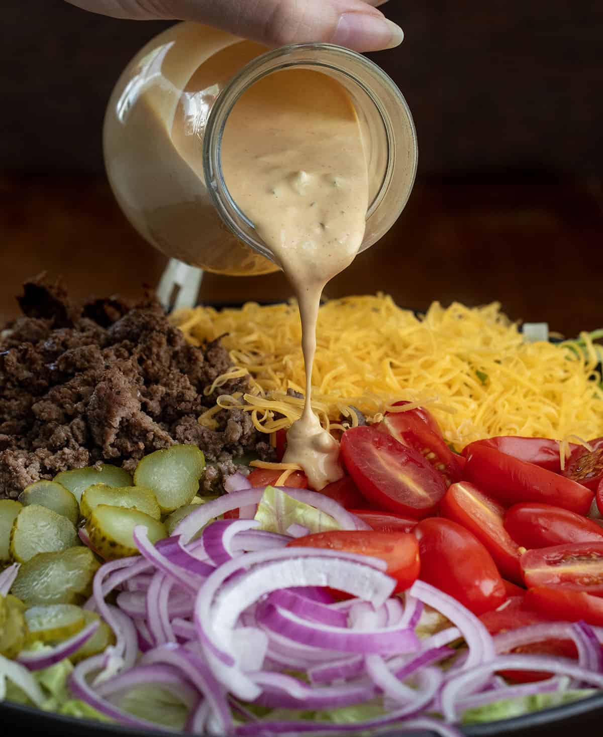 Pouring the Special Sauce dressing over raw ingredients for Cheeseburger Salad Pouring the Special Sauce dressing over raw ingredients for Cheeseburger Salad.