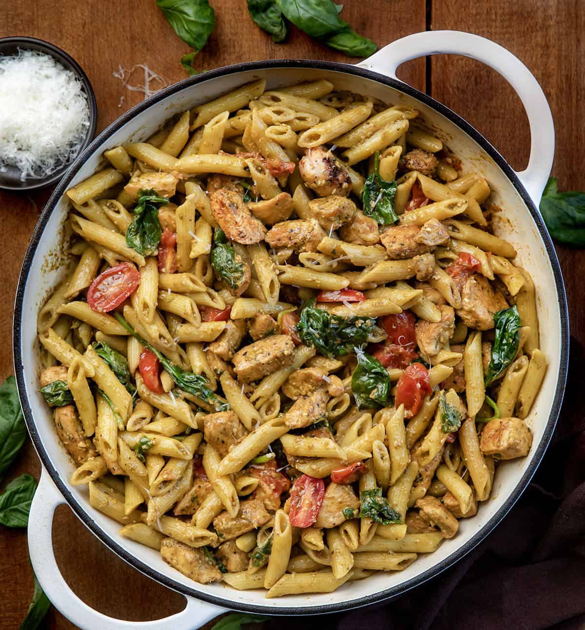 White skillet of Chicken Pesto Pasta on a wooden table from overhead White skillet of Chicken Pesto Pasta on a wooden table from overhead.