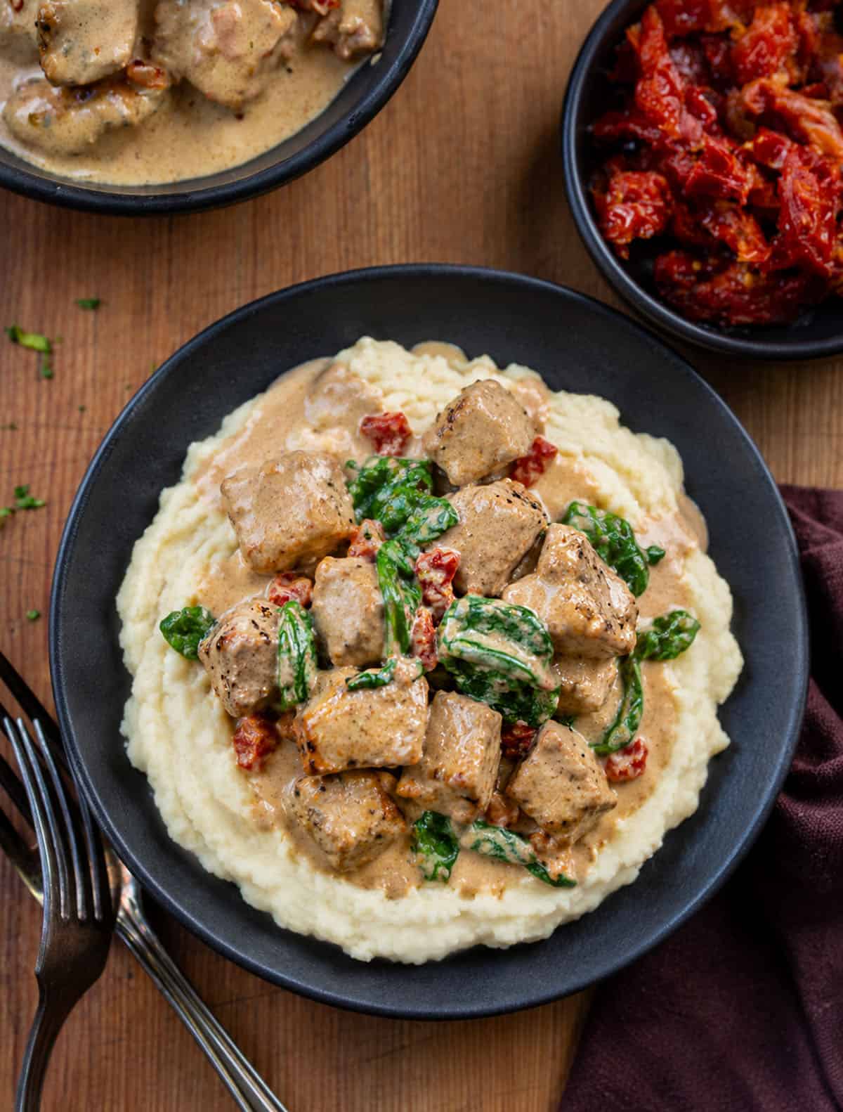 Black bowl filled with mashed potatoes and topped with Creamy Tuscan Pork Bites Black bowl filled with mashed potatoes and topped with Creamy Tuscan Pork Bites.