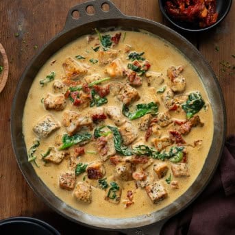 Skillet of Creamy Tuscan Pork Bites on a wooden table from overhead.