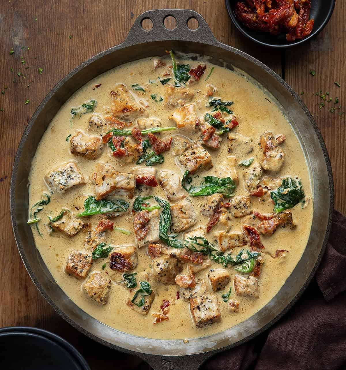 Skillet of Creamy Tuscan Pork Bites on a wooden table from overhead Skillet of Creamy Tuscan Pork Bites on a wooden table from overhead.