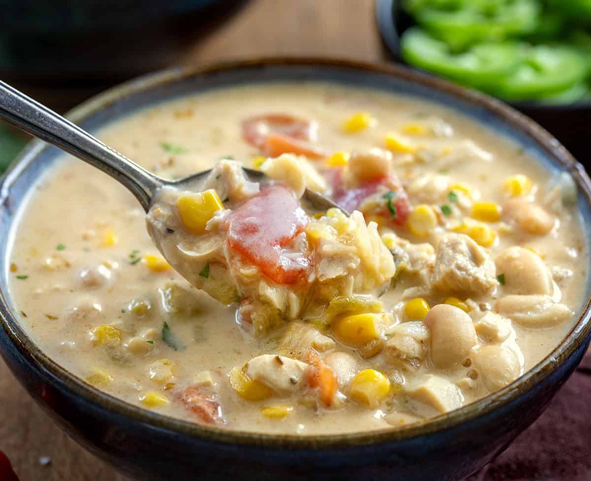 Bowl of Creamy White Bean Chicken Chili with a spoon with soup on it being held above the bowl Bowl of Creamy White Bean Chicken Chili with a spoon with soup on it being held above the bowl.