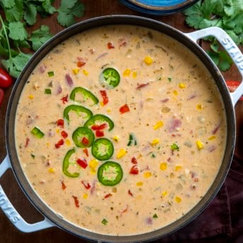 Pot of Creamy White Bean Chicken Chili on a wooden table surrounded by bowls and cilantro and tomatoes.