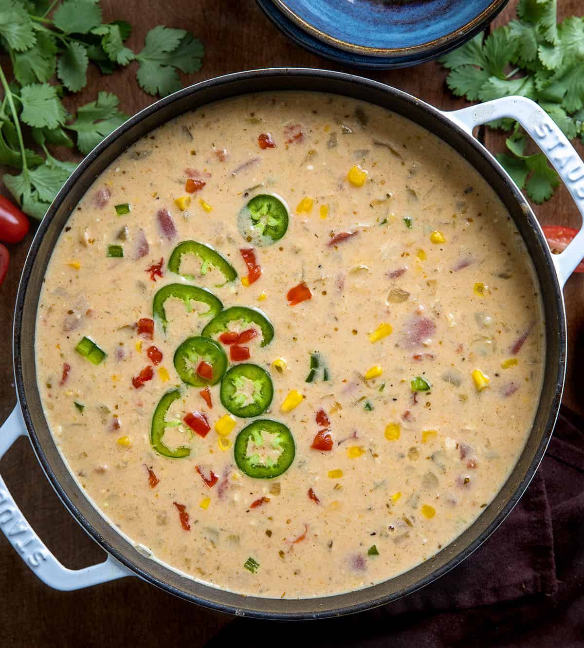 Pot of Creamy White Bean Chicken Chili on a wooden table surrounded by bowls and cilantro and tomatoes Pot of Creamy White Bean Chicken Chili on a wooden table surrounded by bowls and cilantro and tomatoes.