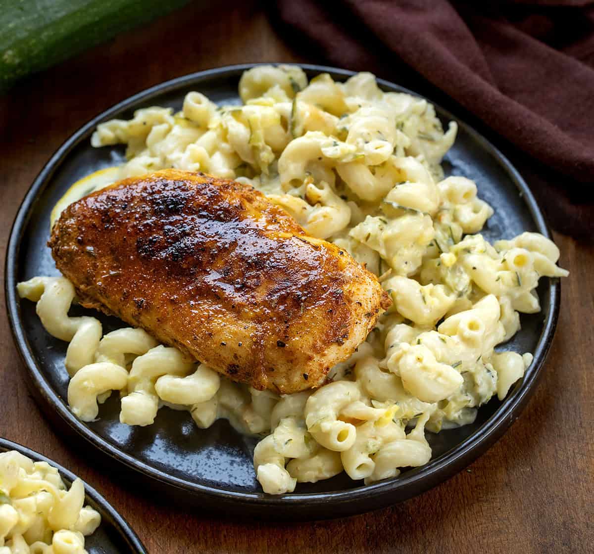 Black plate with Garlic Lemon Chicken Zucchini Pasta on it on a wooden table with fresh zucchini and lemon Black plate with Garlic Lemon Chicken Zucchini Pasta on it on a wooden table with fresh zucchini and lemon.