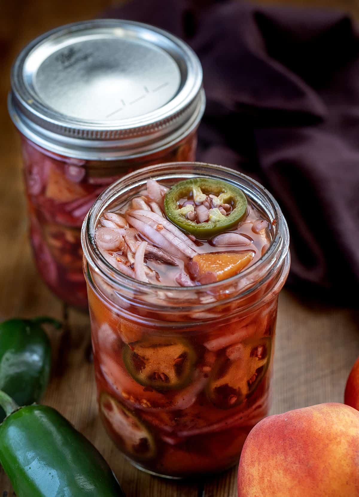 Close up of an opened jar of Jalapeño Peach Pickled Onions on a wooden table Close up of an opened jar of Jalapeño Peach Pickled Onions on a wooden table.