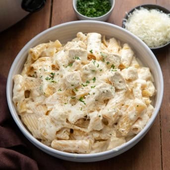 Bowl of Slow Cooker Chicken Alfredo Pasta next to the slow cooker on a wooden table.