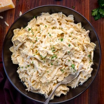 Black serving bowl filled with Slow Cooker Chicken Alfredo Pasta on a wooden table from overhead.
