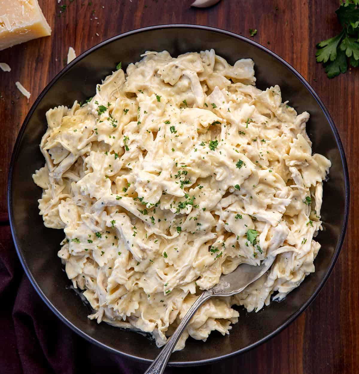 Black serving bowl filled with Slow Cooker Chicken Alfredo Pasta on a wooden table from overhead Black serving bowl filled with Slow Cooker Chicken Alfredo Pasta on a wooden table from overhead.