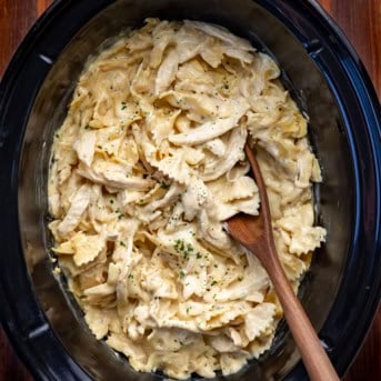 Slow Cooker Chicken Alfredo Pasta with a wooden spoon in it on a wooden table.