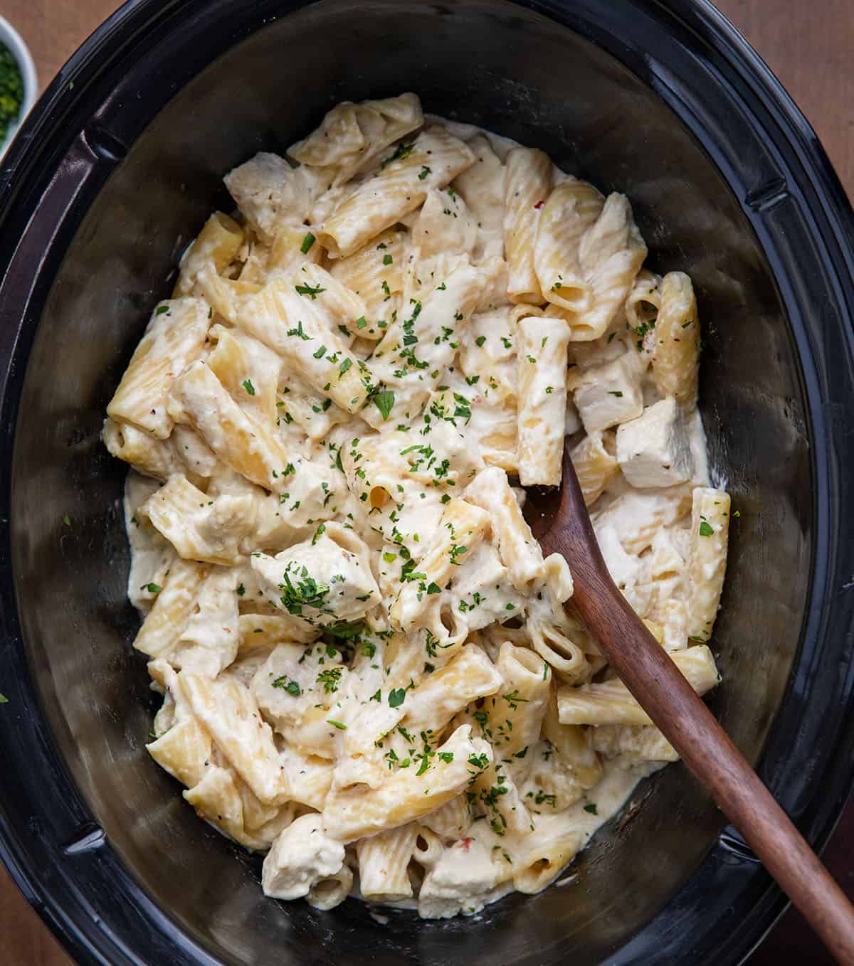 Slow Cooker Chicken Alfredo Pasta with a wooden spoon in it on a wooden table from overhead Slow Cooker Chicken Alfredo Pasta with a wooden spoon in it on a wooden table from overhead.