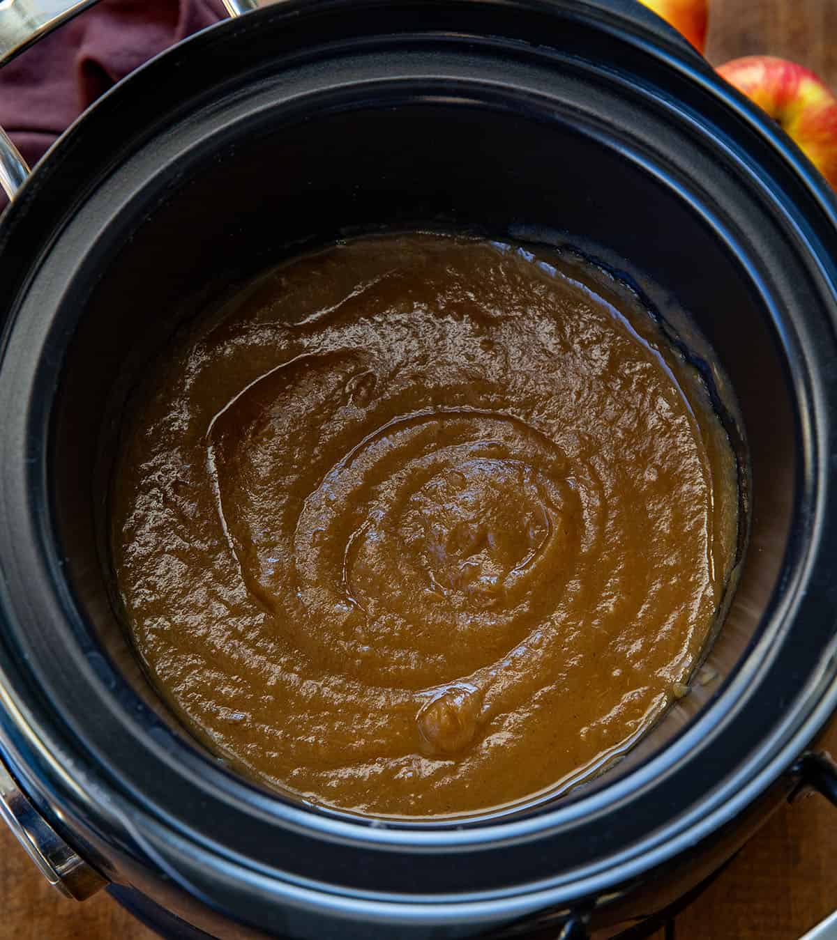 Slow cooker filled with Maple Apple Butter on a wooden table Slow cooker filled with Maple Apple Butter on a wooden table.