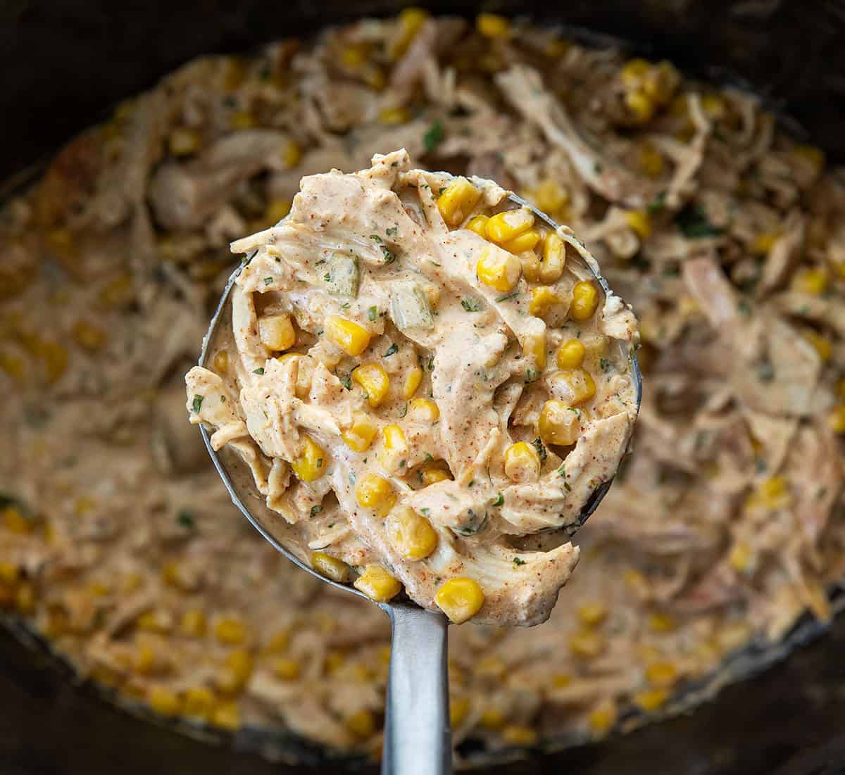 Ladle filled with Slow Cooker Street Corn Chicken being held above the slow cooker Ladle filled with Slow Cooker Street Corn Chicken being held above the slow cooker.