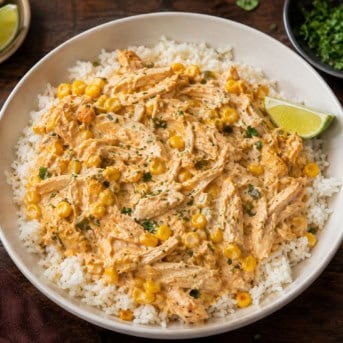 Slow Cooker Street Corn Chicken over rice in a white bowl on a wooden table.
