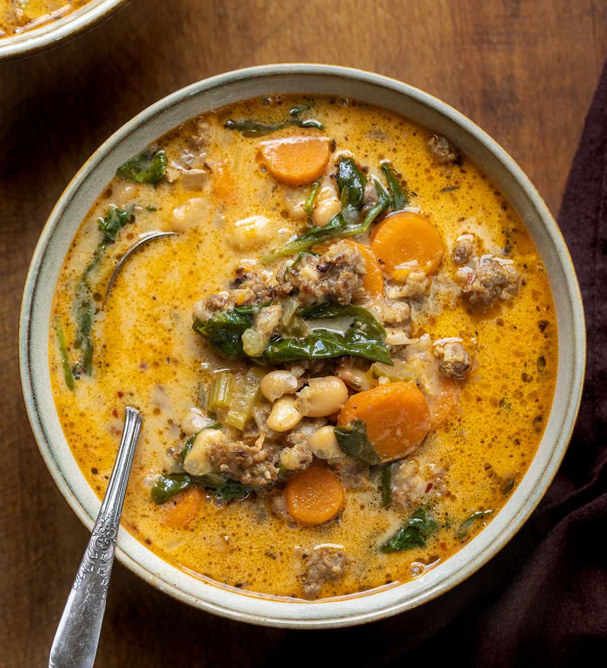 Bowl of Slow Cooker Tuscan White Bean Soup with a spoon in it on w wooden table from overhead Bowl of Slow Cooker Tuscan White Bean Soup with a spoon in it on w wooden table from overhead.
