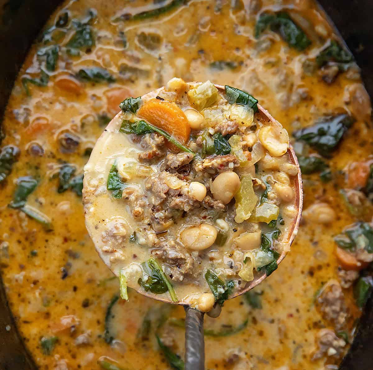 Ladle full of Slow Cooker Tuscan White Bean Soup being held above the crockpot Ladle full of Slow Cooker Tuscan White Bean Soup being held above the crockpot.