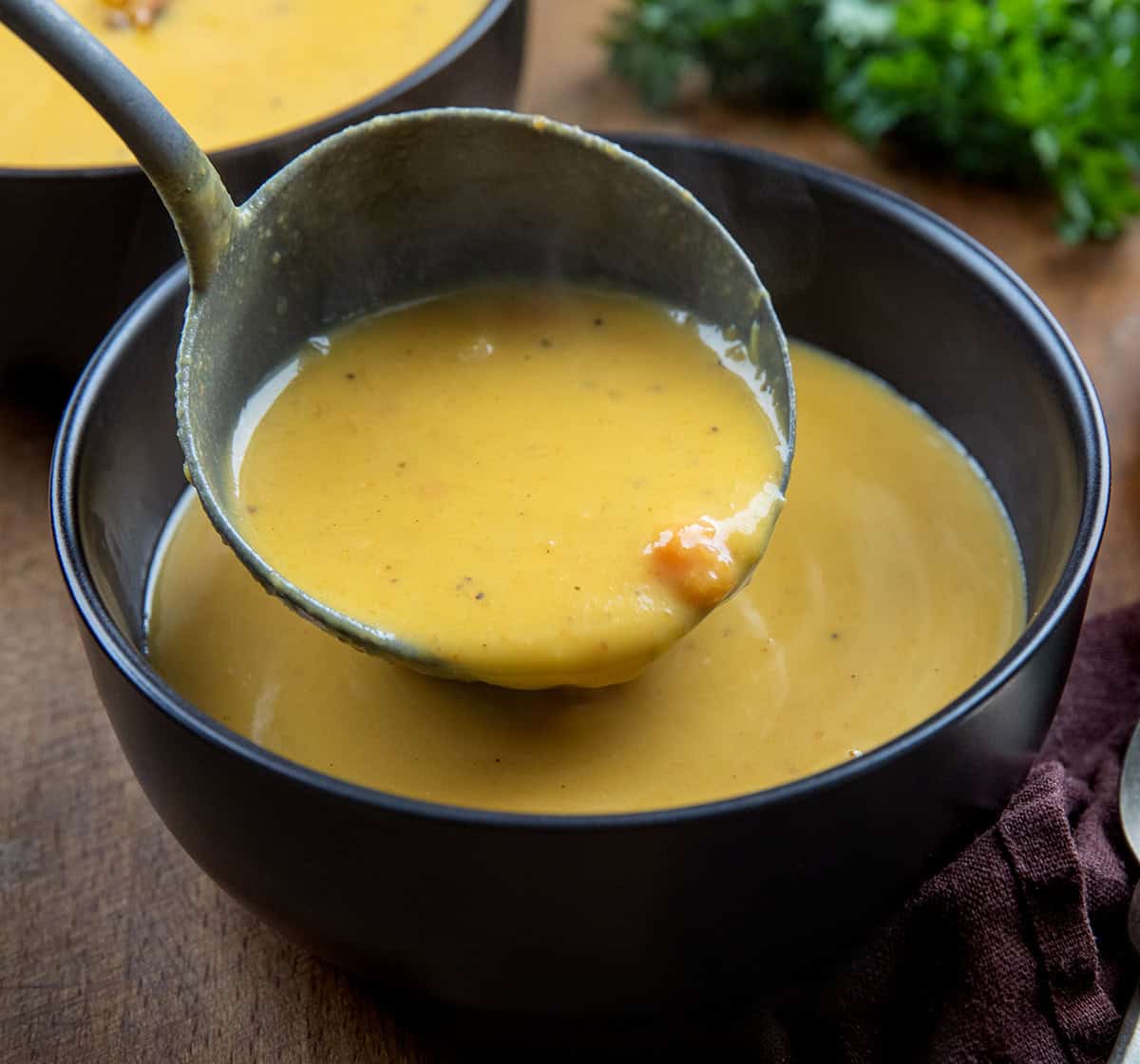 Ladeling Apple Butternut Squash Soup into a black bowl Ladeling Apple Butternut Squash Soup into a black bowl.