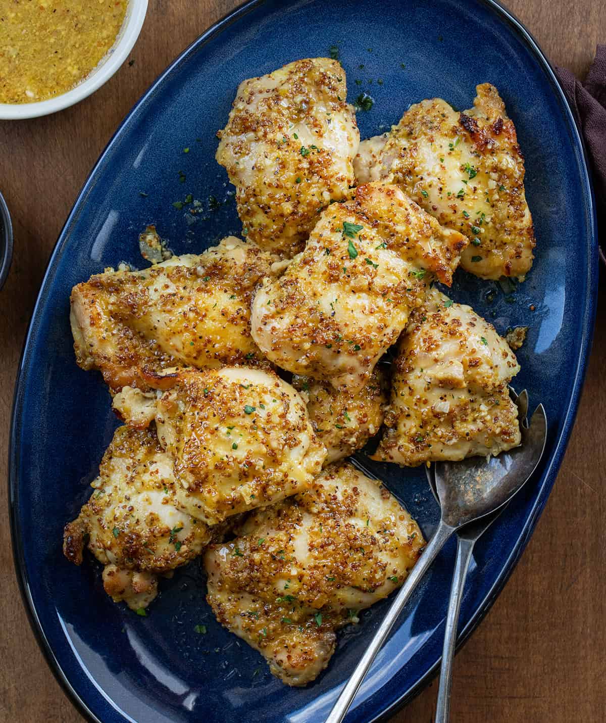 Blue serving platter of Baked Honey Mustard Chicken Thighs on a wooden table from overhead Blue serving platter of Baked Honey Mustard Chicken Thighs on a wooden table from overhead.
