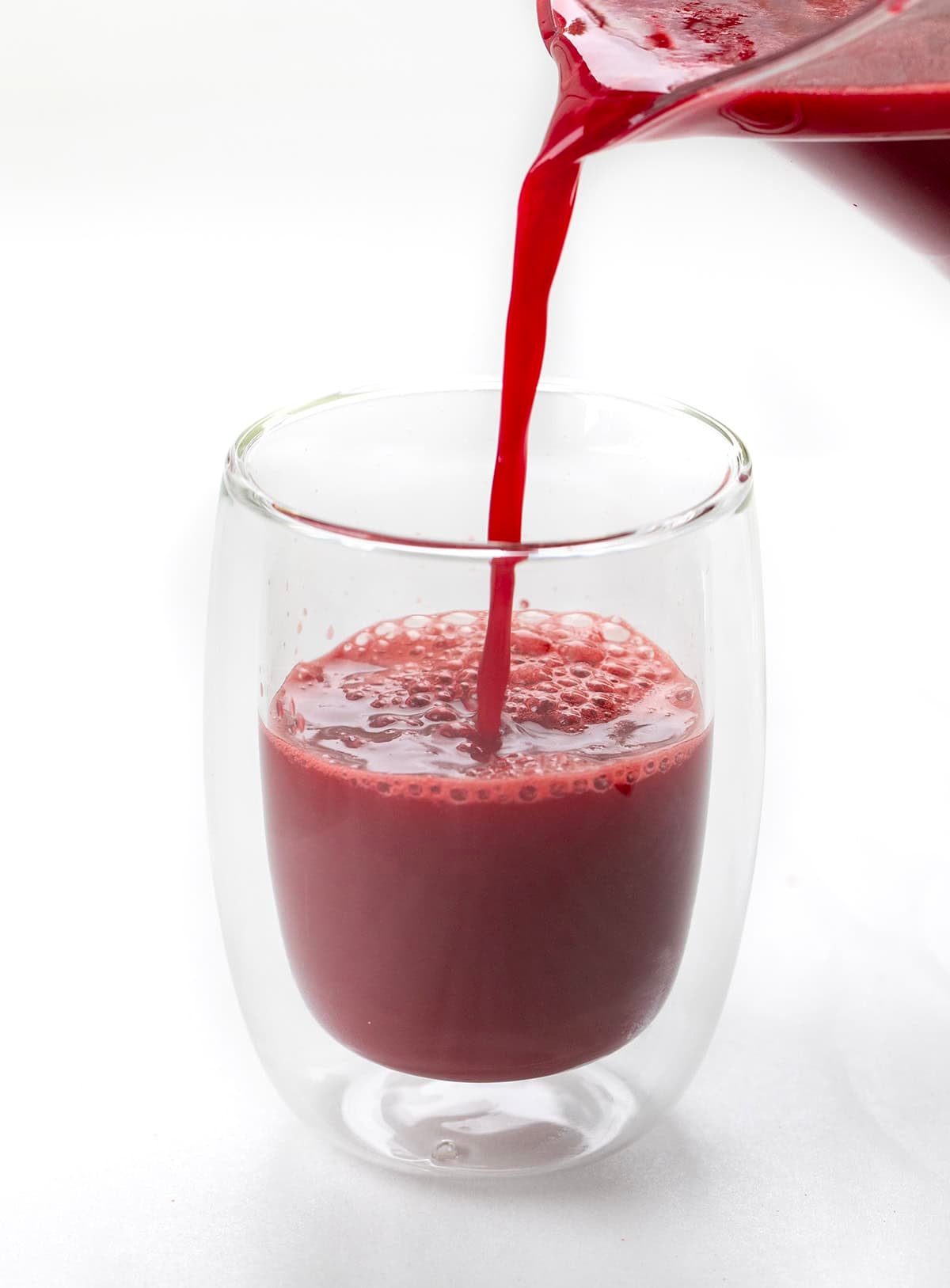 Pouring Beet Raspberry Energy Shot into a glass on a white table.