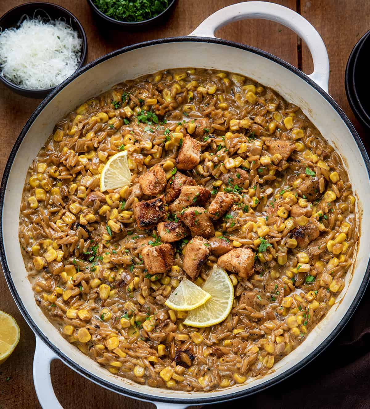 Skillet of Creamed Corn Orzo with Chicken on a wooden table from overhead Skillet of Creamed Corn Orzo with Chicken on a wooden table from overhead.