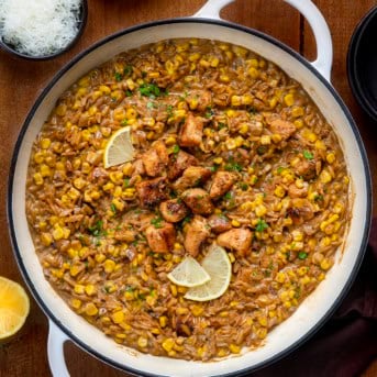 Skillet of Creamed Corn Orzo with Chicken on a wooden table from overhead.
