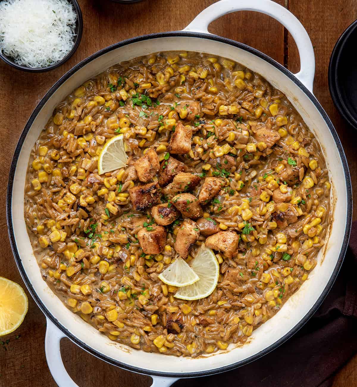 Skillet of Creamed Corn Orzo with Chicken on a wooden table from overhead Skillet of Creamed Corn Orzo with Chicken on a wooden table from overhead.