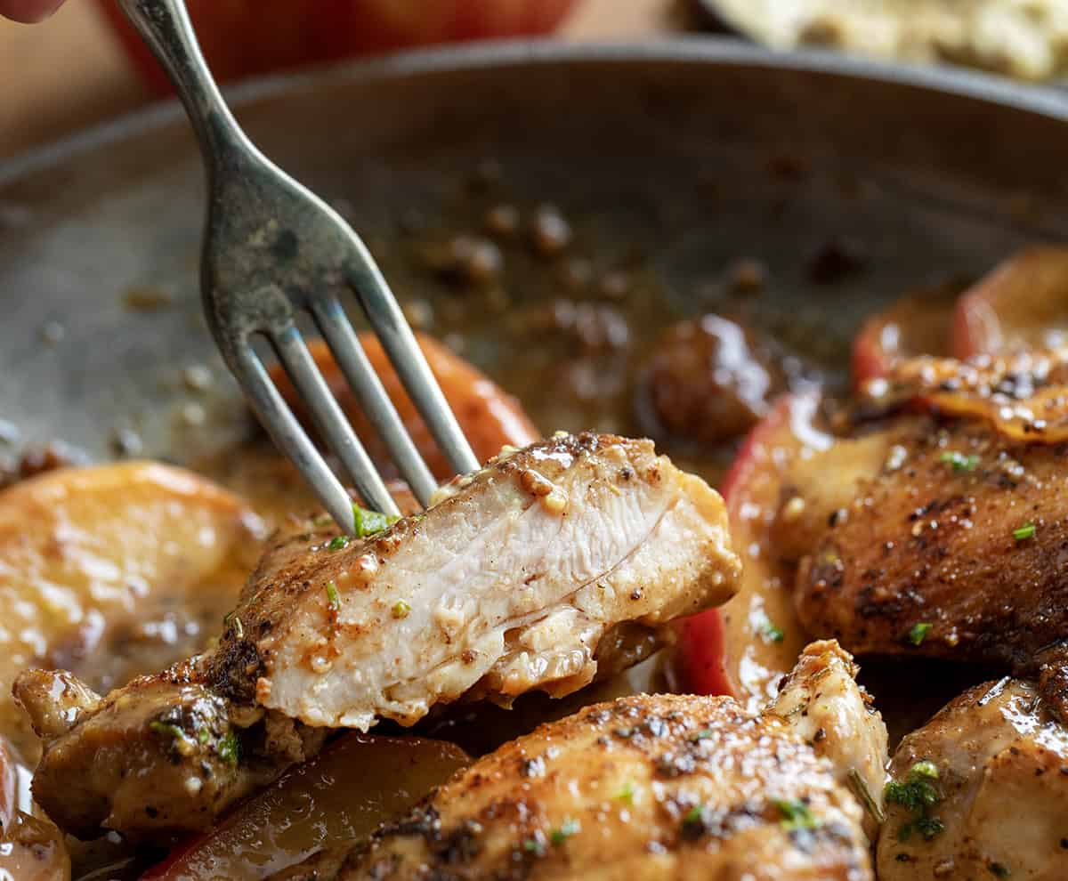Fork with a cut piece of Dijon Apple Shallot Chicken being held above the pan Fork with a cut piece of Dijon Apple Shallot Chicken being held above the pan.
