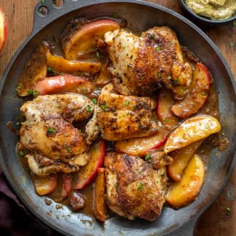 Skillet of Dijon Apple Shallot Chicken on a wooden table from overhead.