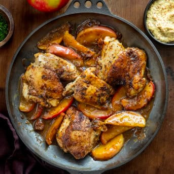Skillet of Dijon Apple Shallot Chicken on a wooden table from overhead.