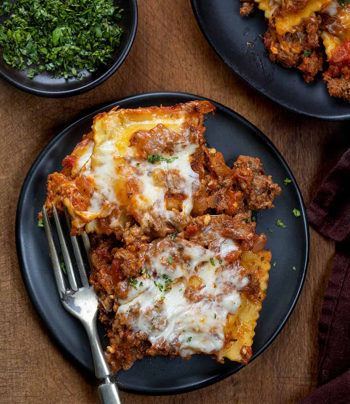 Black plates of Easy Baked Ravioli on a wooden table from overhead Black plates of Easy Baked Ravioli on a wooden table from overhead.
