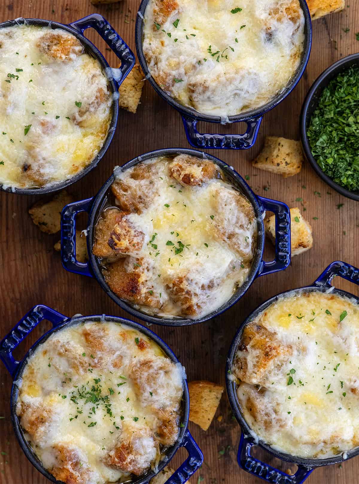 Small blue crocks of French Onion Soup with croutons and melted cheese from overhead on a wooden table Small blue crocks of French Onion Soup with croutons and melted cheese from overhead on a wooden table.
