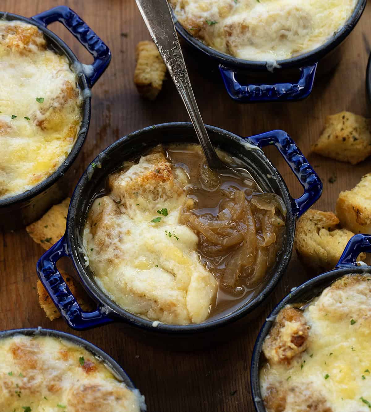 Half eaten bowl of French Onion Soup on a wooden table surrounded by croutons Half eaten bowl of French Onion Soup on a wooden table surrounded by croutons.