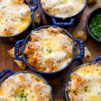 Close up of French Onion Soup in blue crocks on a wooden table.