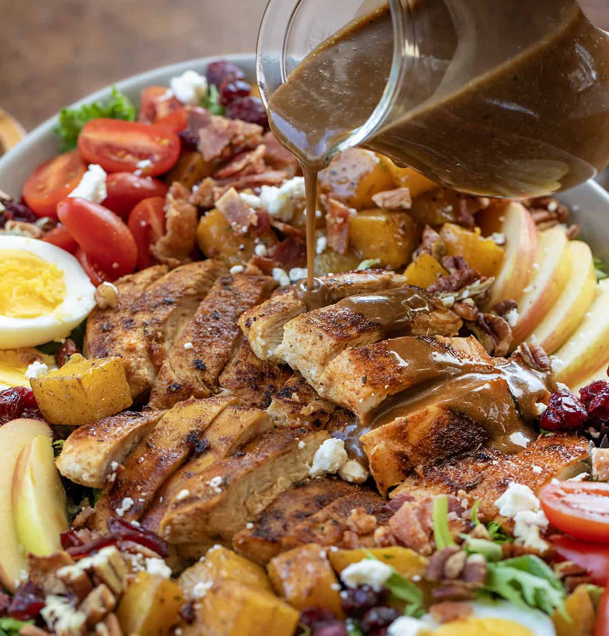 Close up of pouring balsamic vinaigrette over chicken in a Harvest Chicken Salad.