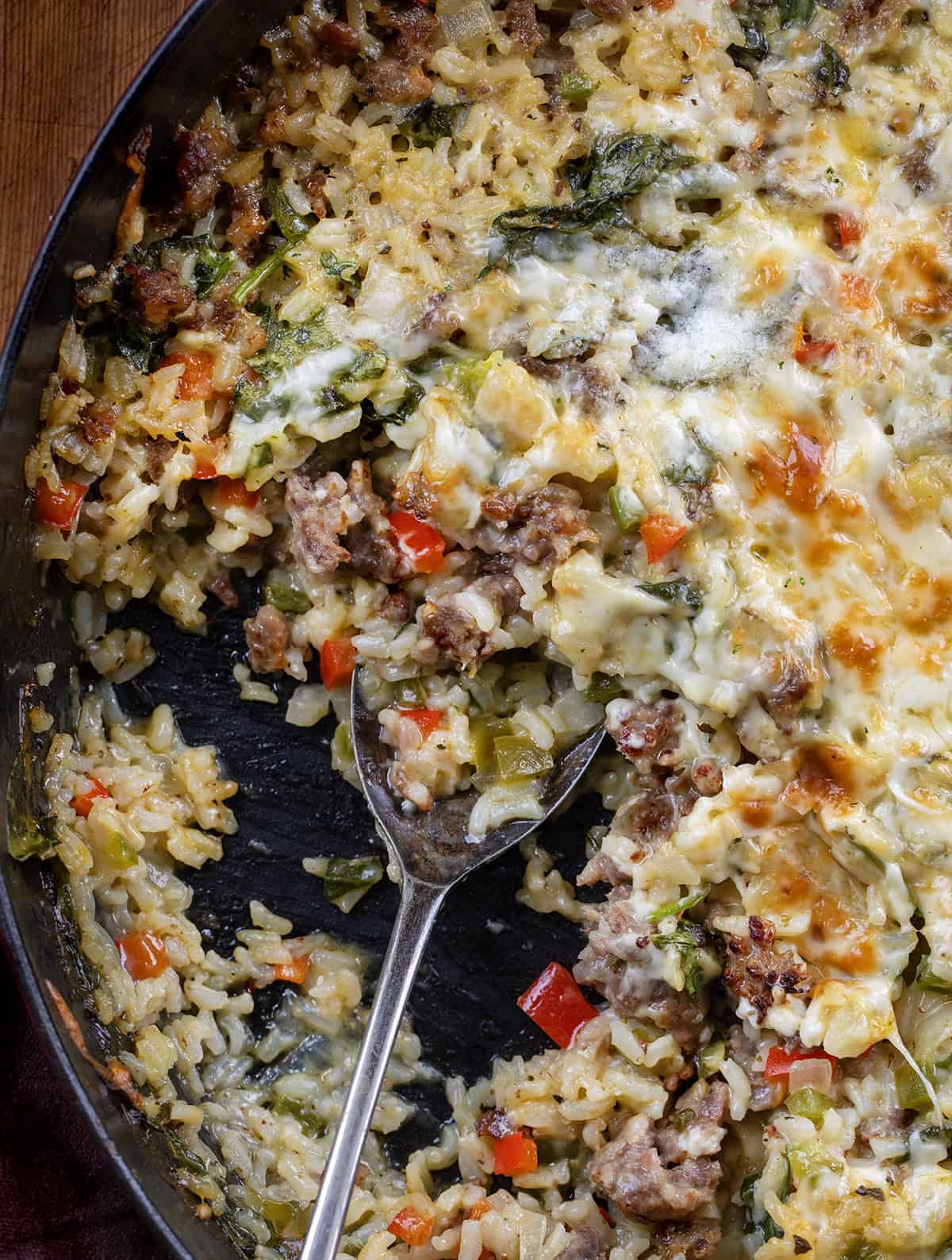 Skillet of Italian Sausage and Rice with a portion missing and a spoon in the pan Skillet of Italian Sausage and Rice with a portion missing and a spoon in the pan from overhead.