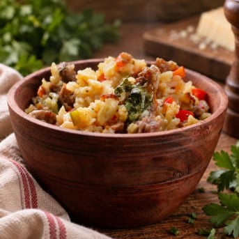 Bowl of Italian Sausage and Rice on a wooden table form parmesan and a towel.