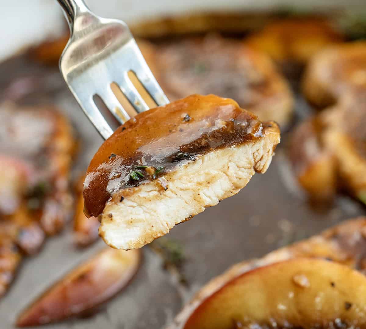 Piece of Peach Balsamic Chicken on a fork being held above the pan Piece of Peach Balsamic Chicken on a fork being held above the pan.