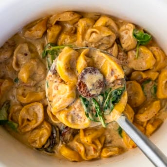 Ladle full of Slow Cooker Kielbasa Tortellini Soup being held above the crockpot.