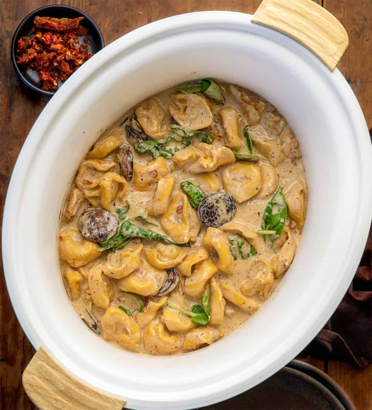 Slow Cooker Kielbasa Tortellini Soup on a wooden table from overhead Slow Cooker Kielbasa Tortellini Soup on a wooden table from overhead.
