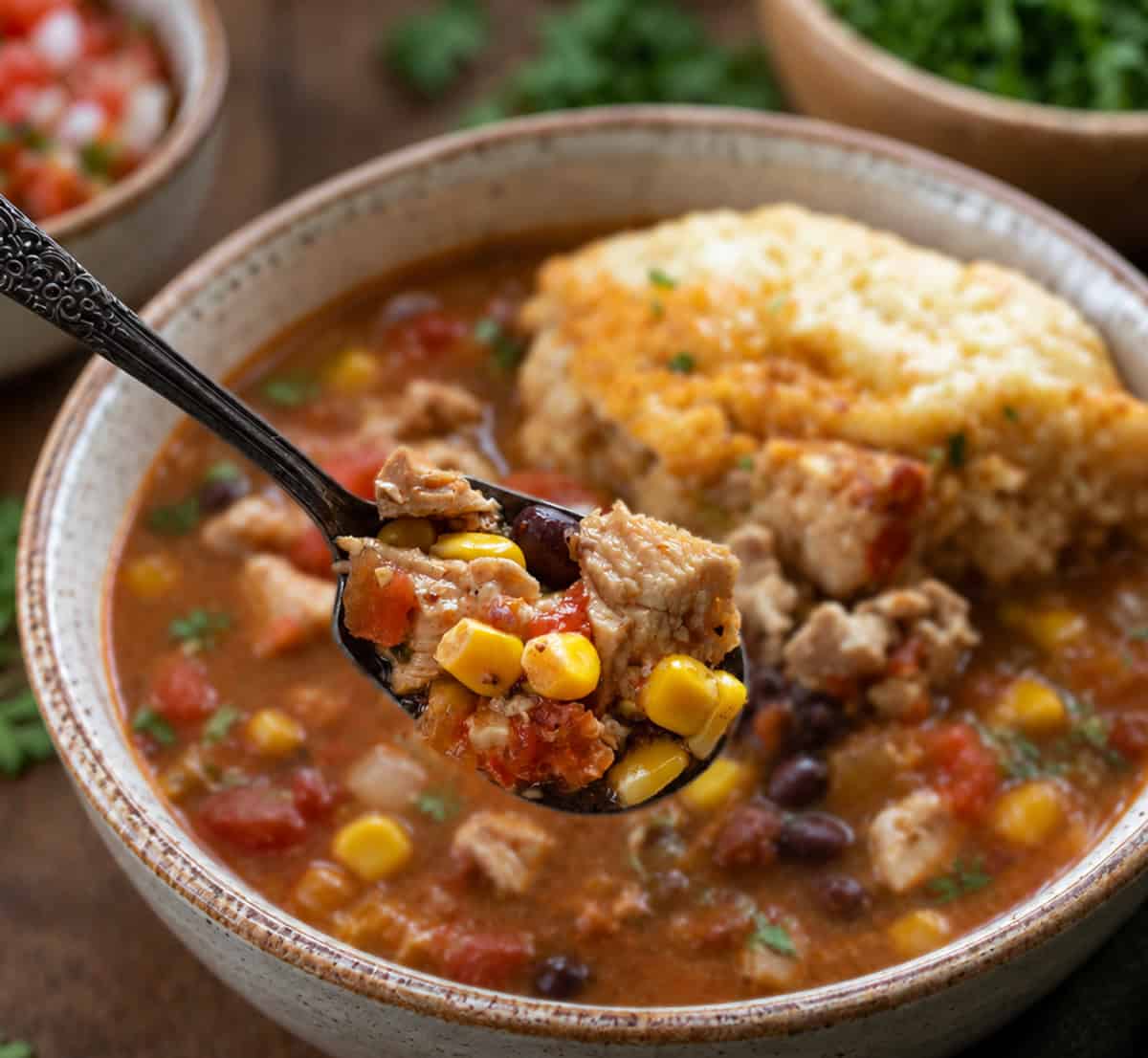 Bowls of Southwest Chicken and Dumplings on a wooden table with a spoonful of the soup being held above the bowl Bowls of Southwest Chicken and Dumplings on a wooden table with a spoonful of the soup being held above the bowl.