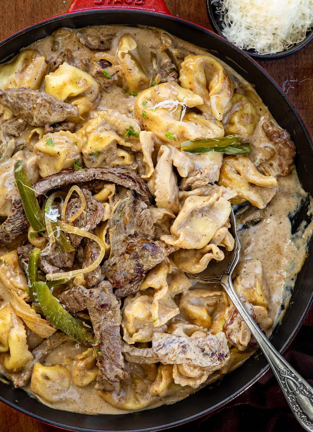 Close up of a skillet of Cheesesteak Tortellini with a serving spoon in it Close up of a skillet of Cheesesteak Tortellini with a serving spoon in it.